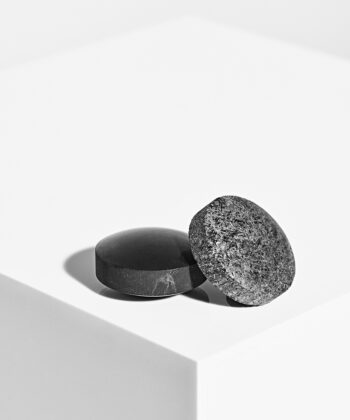 To Harmonizers i lomme størrelse som ligger på en hvid plade med hvid baggrund. dEt er en sort shungit og en grå sæbesten