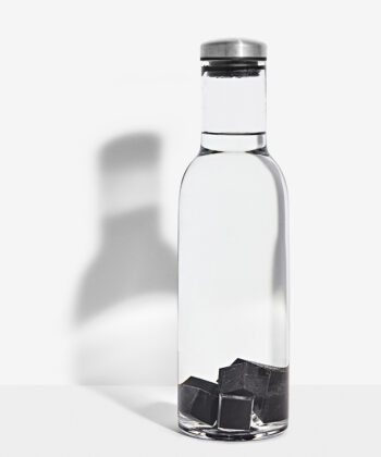 sorte Shungit kuber som ligger i en vandflaske - baggrunden er hvid