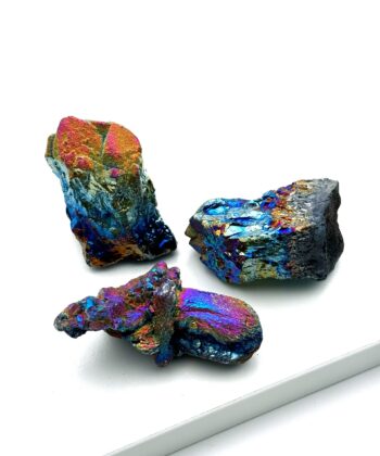 Tre metallisk regnbuefarvede rå krystaller på hvid baggrund