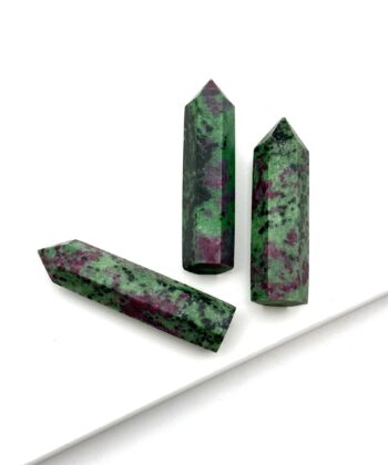Tre grønne søjler af halvædelsten med lilla og sorte detaljer på hvid baggrund