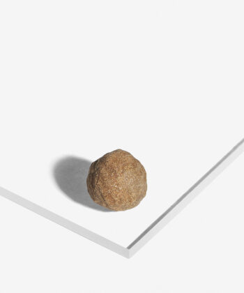 Rund gylden Moqui Marble sten med ru overflade fotograferet på hvid baggrund