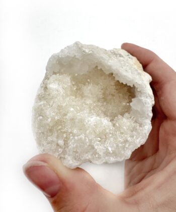 Lys geode klynge med hvide krystaller holdt i hånd på hvid baggrund