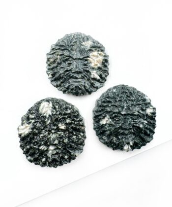 Grøn rund medaljon med udskåret ansigts mønster i midten på hvid baggrund